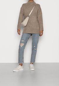 Übergroßer, gerippter brauner Pullover, hellblaue, verwaschene Jeans mit Rissen und weiße Sneakers. Minimalistische beige Umhängetasche mit Kettenriemen.