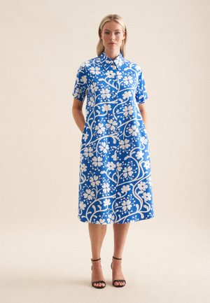 Short-sleeve blue dress with a floral white pattern, button-up front, collared neckline, and side pockets. Smooth cotton fabric.
