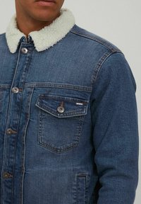 Chaqueta de mezclilla con un ligero cuello forrado de piel, lavado azul oscuro, cierre con botones, bolsillo en el pecho con botón y detalles de costura en contraste.