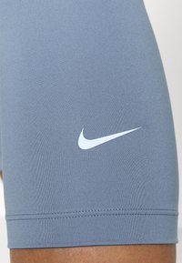 Harmaat urheilushortsit, joissa on istuva malli ja sileä kangas. Vasemmassa reidessä on valkoinen Nike-logo ja litteä vyötärönauha.