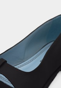 Κοντινό πλάνο ενός μαύρου επίπεδου παπουτσιού με μπλε εσωτερική επένδυση και εμφανείς ραφές κατά μήκος της άκρης της εσωτερικής σόλας.