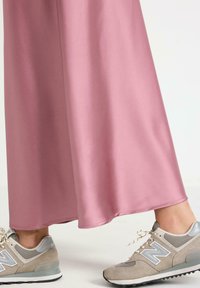 Gonna lunga in satin rosa abbinata a sneakers New Balance grigie con texture in mesh e suede, accentuate da un logo bianco.