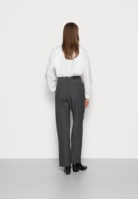 Grijze op maat gemaakte broeken met een hoge taille en rechte pijpen, gecombineerd met een witte oversized blouse. Zwarte enkellaarsjes maken de look compleet.