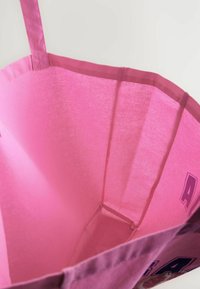 Borsa a tracolla in tessuto rosa con un ampio interno, texture liscia e cuciture rinforzate, e un dettaglio esterno a motivo.