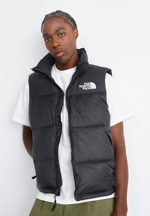 Black puffer vest with high collar, front zip closure, and logo on the left chest. Lightweight fabric, quilted design, and no sleeves.