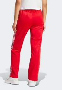 Pantaloni sportivi rossi realizzati in tessuto liscio, con una vestibilità comoda, vita elastica e tre strisce bianche lungo i lati.