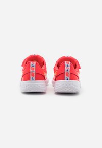 Red athletic shoes with white soles. Features a padded collar, velcro strap, and patterned heel tabs with branding. Textured rubber sole.