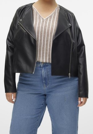 Personne portant une veste de motard en cuir noir sur un t-shirt beige et blanc à rayures et un jean bleu taille haute, sur un fond blanc.