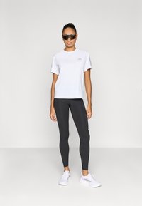 Fehér rövid ujjú atlétikai ing szürke részletekkel, fekete leggingszel párosítva. A fehér atlétikai cipő egészíti ki az egyszerű, minimalista stílusú öltözéket.