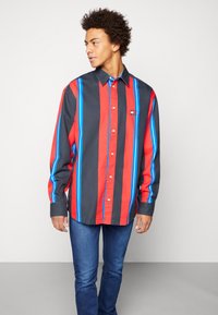 Czerwona, czarna i niebieska koszula z guzikami w paski z bawełnianego materiału, z kołnierzykiem, długimi rękawami i małym logo na piersi.