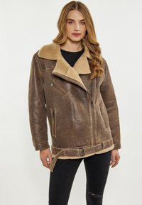 Giacca di pelle marrone con colletto e fodera in shearling beige, chiusura zip, tasche laterali e vita con cintura. Design a trama, fit rilassato.