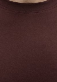 Gros plan d'une texture de tissu marron avec un col rond et des coutures visibles sur un vêtement.