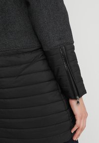 Czarna ocieplana kurtka zimowa z szarym wełnianym górnym panelem, wyposażona w zapinany na zamek rękaw i pikowaną teksturę na dolnej części.