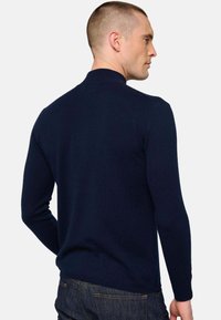 Marineblauer Strickpullover mit hohem Kragen, langen Ärmeln und taillierter Passform, ausgestattet mit glatter Textur und minimalen Nähten.