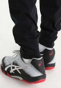 Des chaussures de sport noires et rouges avec une tige en maille et des accents gris, un logo blanc distinctif, une semelle rembourrée et un panneau de talon texturé.