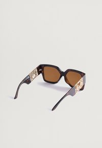 Γυαλιά ηλίου από καφέ χελώνα με χοντρή σχεδίαση, καφέ φακούς και χρυσές γεωμετρικές λεπτομέρειες στα πλάγια. Κ textured πλαστικό σκελετό.