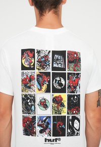Camiseta blanca de algodón con un estampado gráfico multicolor de Spider-Man en 12 paneles cuadrados, cada uno mostrando diversas escenas y estilos de cómic.