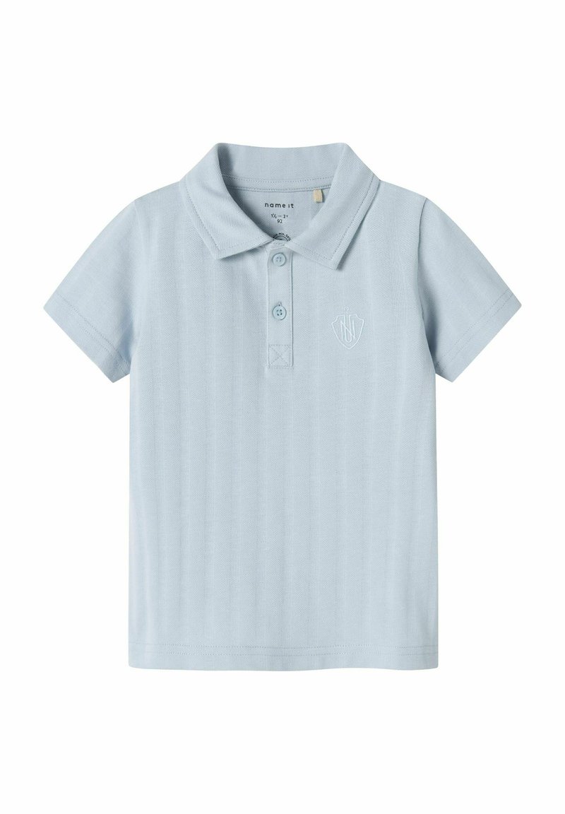 Polo shirt bleu clair à manches courtes, en tissu texturé, avec un col, trois boutons, et un logo brodé sur la poitrine.