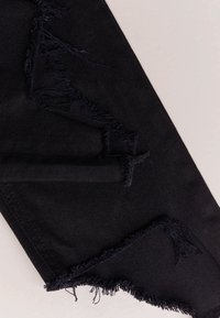 Tela de mezclilla negra con bordes deshilachados, que presenta una superficie texturizada y un diseño de dobladillo sin terminar.