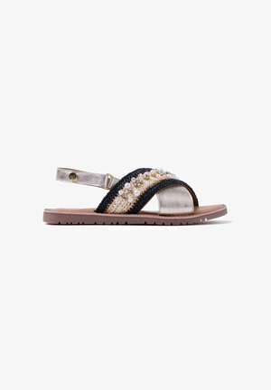 Sandalias con una correa tejida negra, detalles metálicos y crema. Presentan cuentas y una suela plana de goma con un patrón texturizado.