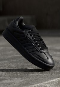 Svart sneakers i läder med slät yta, rund tå och snörning, med subtil logotyp och tre randiga detaljer på sidan.