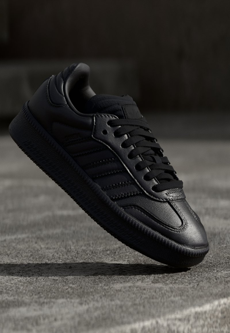 Svart sneakers i läder med slät yta, rund tå och snörning, med subtil logotyp och tre randiga detaljer på sidan.