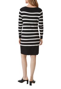 Gestreiftes Strickkleid in Schwarz-Weiß mit langen Ärmeln, Bootsausschnitt und schwarzem, einfarbigem Saum; kombiniert mit schwarzen High-Heel-Mules.