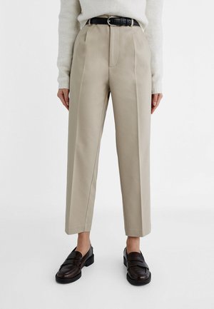 Beige hoge taille broek met frontplooien, een zwarte riem, gecombineerd met zwarte loafers en een wit trui met lange mouwen.