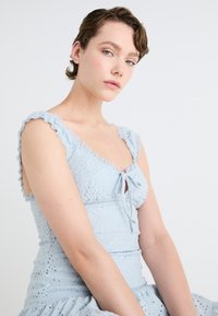 Svijetloplava haljina od teksturirane tkanine s cvjetnim uzorkom, volančićima na naramenicama i detaljem mašne na izrezu.