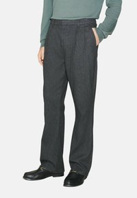 Gray pleated trousers with a straight-leg fit, made of textured fabric, featuring side pockets and worn with black loafers.