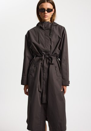 Abrigo largo de color gris oscuro hecho de material impermeable, con capucha, cordones ajustables, cinturón para atar y bolsillos laterales.