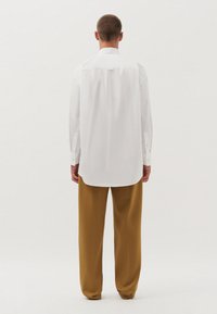 Witte langslavende shirt met een standaard kraag, knoopmanchetten en een afgeronde zoom, gecombineerd met losse mosterdgele broeken.