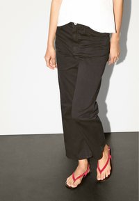 Black wide-leg trousers made of cotton, featuring a button closure and classic five-pocket design, paired with pink thong sandals.