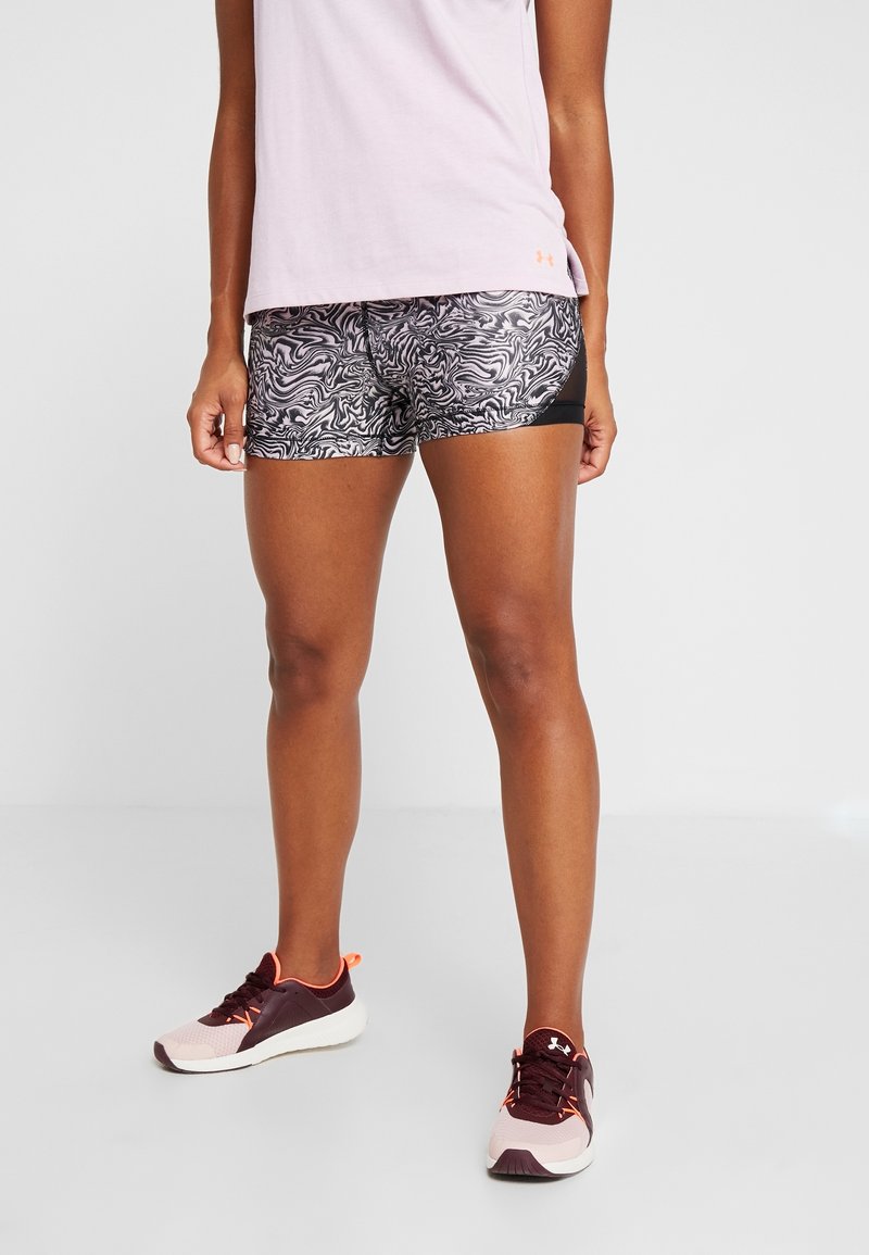 Personne portant un short de sport à motifs noir et blanc, un haut rose clair et des chaussures de course rose foncé et blanc, debout sur un sol clair.