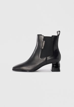 Black leather ankle boot with elastic side panels, pointed toe, and a sculpted block heel. Features a pull tab and logo detail on the side.