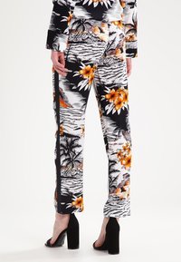 Pantalons à motifs floraux en noir, blanc et orange. Présentent une texture lisse, une coupe ajustée et des fentes latérales.