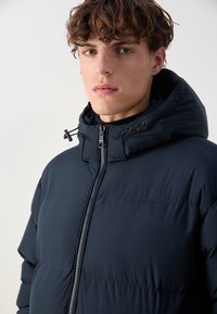 Navy puffer jacket with a zip closure, adjustable hood, and quilted design. Features a smooth texture and a modern fit.