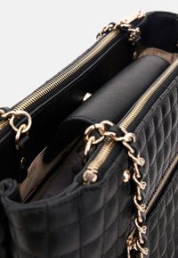 Borsa a tracolla nera trapuntata con hardware dorato, caratterizzata da doppi zip e una tracolla a catena. Interno in pelle liscia con un ampio scomparto.
