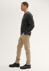 Dunkelgrauer Pullover, beiger Cargo-Hose mit mehreren Taschen und schwarze Knöchelstiefel. Glatte Textur und figurbetontes Design. Einfach und funktional.