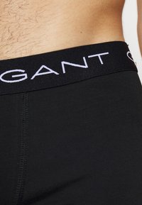 Fekete pamut boxer alsónadrág széles elasztikus derékpánttal, amelyen fehér "GANT" logó található. Sima textúra és testhez simuló kialakítás.