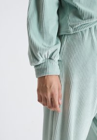 Loungewear côtelé vert menthe avec des poignets froncés. Le tissu a une finition douce et texturée, offrant un look et une sensation confortables.