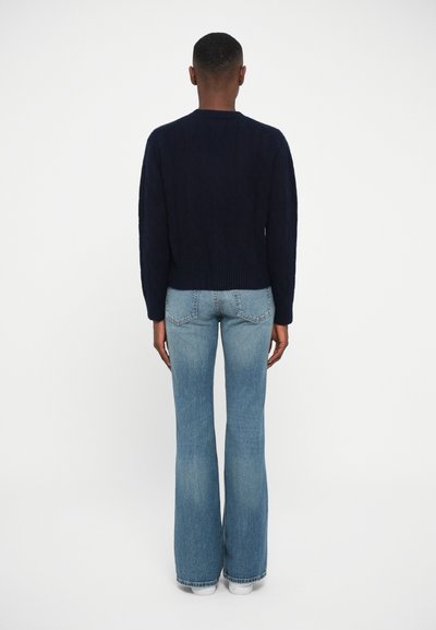 Navy knitted sweater with a round neckline and ribbed hem, paired with light blue flared jeans featuring back pockets and a faded texture.