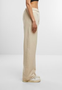 Beige Jogginghose mit elastischem Bund und Kordelzug, mit einem geraden Schnitt. Tragen mit weißen Sneakers, die einen Textdetail zeigen.