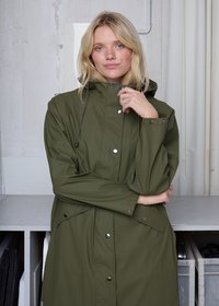 Alyvuogių žalia lietpaltis su gaubtu, su spaudėmis ir reguliuojamais raišteliais. Lygus paviršius, kelių ilgio dizainas ir kišenės šonuose.