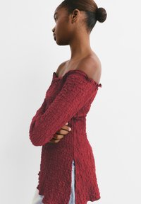 Top off-the-shoulder di un rosso intenso, con maniche lunghe e bordi arricciati, dotato di fessure laterali, realizzato in un tessuto elasticizzato.