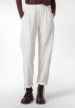 Pantalons blancs amples avec une taille élastique, dotés de plis et de bas roulés, associés à des bottes bordeaux à lacets.