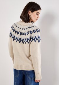 Suéter de punto en beige con un cuello con patrón que presenta acentos en azul, azul marino y azul claro. Corte relajado con puños y dobladillo acanalados.