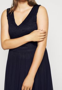 Marinblå klänning med en spetsliv och V-ringning. Kjolen är flödande och har ett strukturerat tyg som ger dimension.