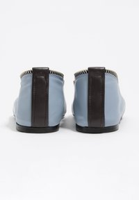 Skórzane buty w jasnym niebieskim kolorze z ciemnobrązowym obcasem i detalami. Posiadają metaliczny zamek błyskawiczny wzdłuż górnej krawędzi. Gładka faktura.