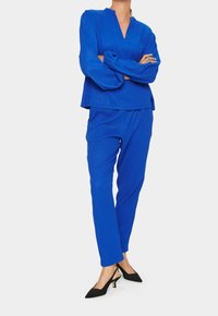 Completo blu in due pezzi con texture, composto da una maglietta a maniche lunghe con scollatura a V e vestibilità ampia, abbinata a pantaloni slim-fit e tacchi neri.